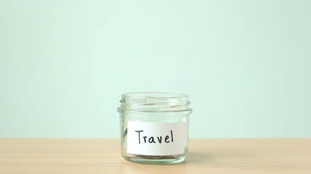 Woman hand putting coins in to saving money jar for travel.
