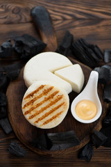 Whole grilled cheese in a rustic wooden setting with charcoals, vertical shot