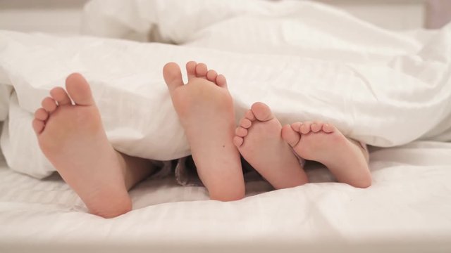 Children's feet moving under blanket. Kids are lying in bed.