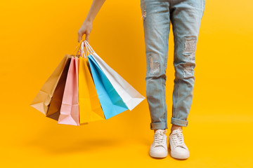 an image of legs, a woman after shopping stands with a lot of multi-colored bags, on a yellow background