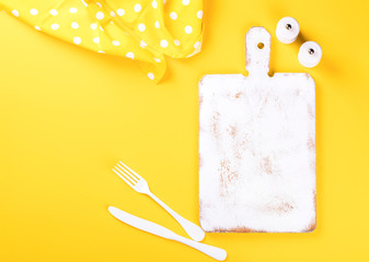 Kitchen chopping wooden board of white color on a bright yellow background. Concept of cooking....