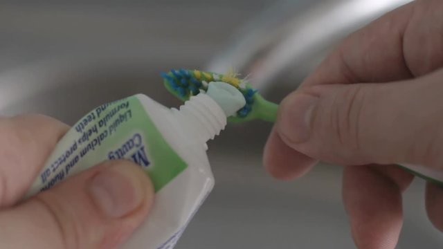Squeezing toothpaste on a green toothbrush