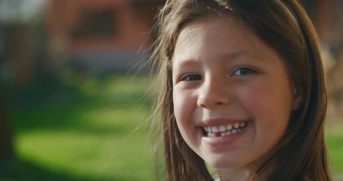 Authentic shot of cute little girl smiling in camera with decayed teeth outside her house on a sunny day.