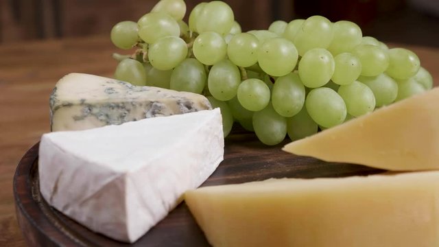 Gouda, brie and dorblu cheese served with white grapes. Variety of cheeses on a wooden tray and wooden background.