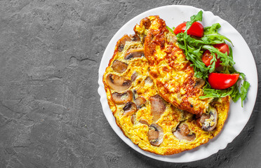 omelette with mushrooms and arugula salad in white plate on Dark grey black slate background