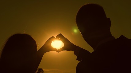 sun in hand. teamwork of a loving couple. couple in love shows heart symbol with hands. Bride and groom making a heart with their hands against a beautiful sunset on horizon. happy family concept