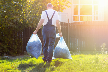 Gardener in uniform carries compost in bags after cleaning the ground.the employee in the sunlight