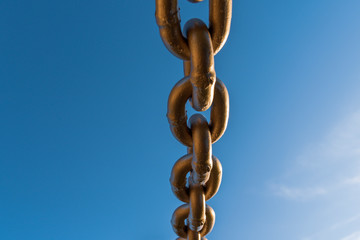 Heavy gold chain from below with blue sky above.