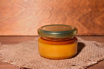 glass jar with honey closed by a cover on a wooden background