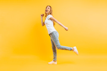 Full length, positive girl walking on a yellow background.