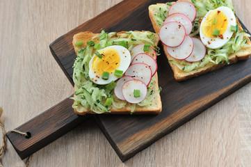 Toasts with hard-boiled egg, fresh cucumber and radish slices. The concept of healthy eating. Light background. Close-up. View from above.