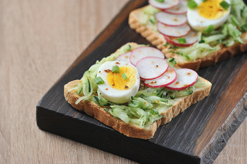 Toasts with hard-boiled egg, fresh cucumber and radish slices. The concept of healthy eating. Light background. Close-up. Free space to place text.