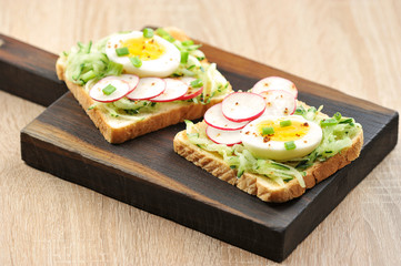 Toasts with hard-boiled egg, fresh cucumber and radish slices. The concept of healthy eating. Light background. Close-up.