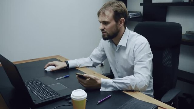 aggressive businessman looks into the phone and computer and aggressively throws out a glass of coffee, angry man, concept of passive aggression at work, slow motion