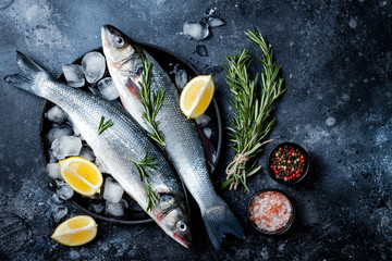 Fresh raw seabass fish on black stone background with spices, herbs, lemon and salt. Culinary seafood background with ingredients for cooking. Top view