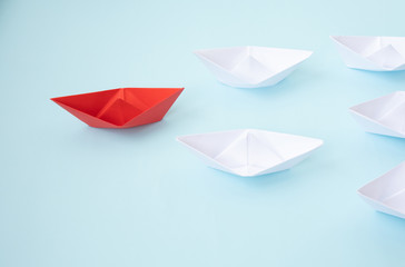 Leadership concept. Red leader paper ship leading among white on blue background.