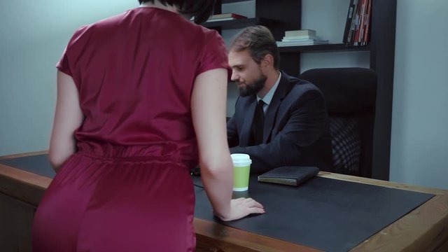 bearded businessman sitting in the office at the laptop, girl in red is trying to seduce the boss, slow motion.