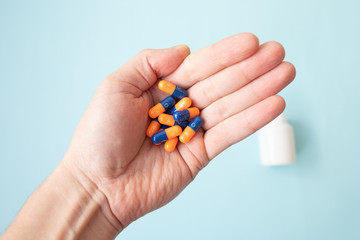 Close-up shot of a hand holding color pills on blue background.