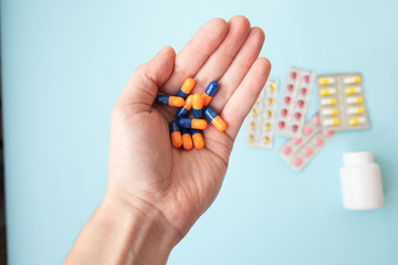 Close-up shot of a hand holding color pills on blue background.