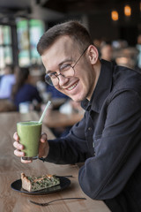 Handsome little bearded man holding fork eating in cafe and smiling looking at camera