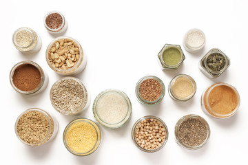 Top view of jars with grains, seeds, legumes, flours and various food ingredients. Healthy food concept.