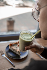 Young stylish man enjoys a cake and a drink while sitting in a cafe with large windows
