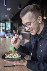 Young stylish man enjoys a cake and a drink while sitting in a cafe with large windows