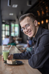 Young stylish man enjoys a cake and a drink while sitting in a cafe with large windows