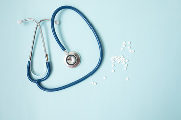 Pills in form of heart next to stethoscope on blue background. Medicine concept.
