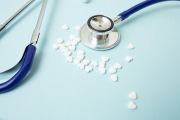 Pills in form of heart next to stethoscope on blue background. Medicine concept.