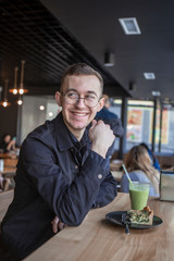 Young stylish man enjoys a cake and a drink while sitting in a cafe with large windows