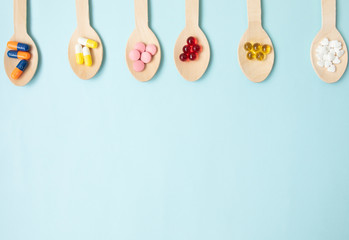 Variety of vitamin pills in wooden spoon on blue background. Healthcare concept. 