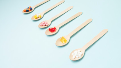 Variety of vitamin pills in wooden spoon on blue background. Healthcare concept. 