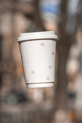 Paper cup of coffee with them frozen in the air on a background blur park. Copy space