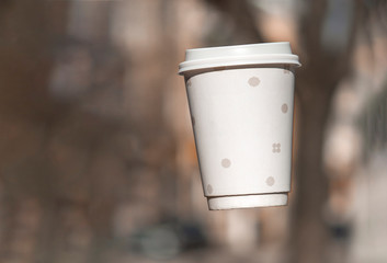 Naklejka na ściany i meble Paper cup of coffee with them frozen in the air on a background blur park. Copy space