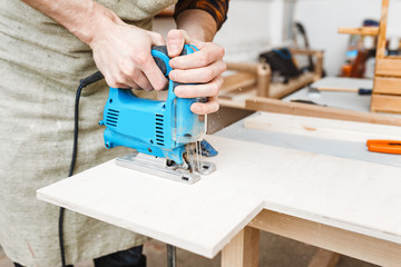 man carpenter working with a jigsaw on wood in the workshop
