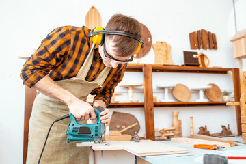 man carpenter working with a jigsaw on wood in the workshop
