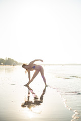Fototapeta na wymiar Yoga silhouette at sunset on the sea shore. woman practices yoga and meditates on the beach