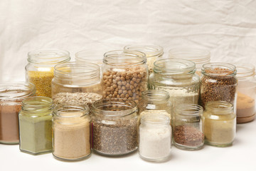 Many jars with grains, seeds, legumes, flours and various food ingredients. Healthy food concept.