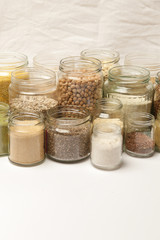 Many jars with grains, seeds, legumes, flours and various food ingredients. Healthy food concept.