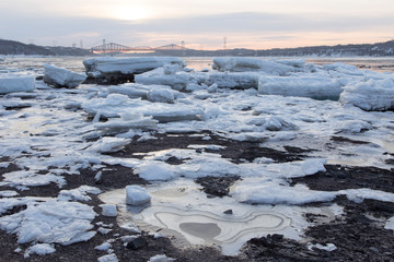 Late winter blue hour morning view of ice sheets and chunks on the banks of the St. Lawrence river and of the Pierre-Laporte and Quebec bridges in the background, Quebec City, Quebec, Canada