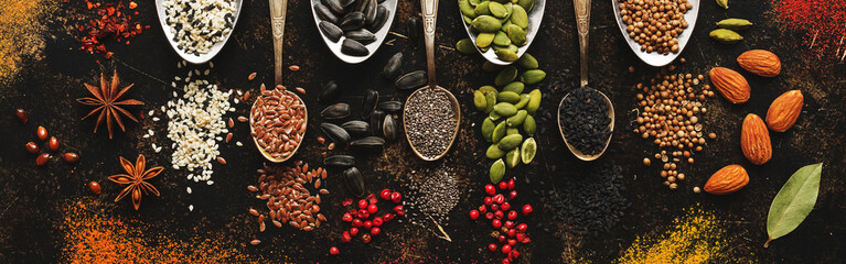 A variety of spices, seeds, nuts in spoons on a dark rustic background. Top view, flat lay.
