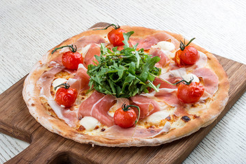 Pizza with Parma ham, mozzarella and cherry tomatoes on a wooden board
