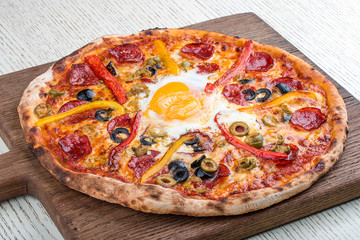 Pizza with salami, sweet pepper, egg and olives on a wooden board