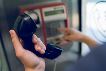 Close up on hand of a young man holding a phone at public call box dialing number