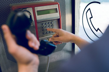 Close up on hand of a young man holding a phone at public call box dialing number