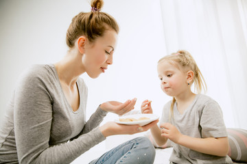 Young mother and her little daughter at home at sunny morning. Soft pastel colors. Happy family time on weekend. Mother's Day concept. Family, love, lifestyle, motherhood and tender moments concepts.