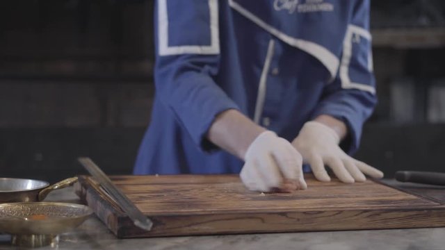 Hands of skillful man in blue chef uniform preparing raw minced meat for lula kebab in modern restaurant. Large grill oven in the background