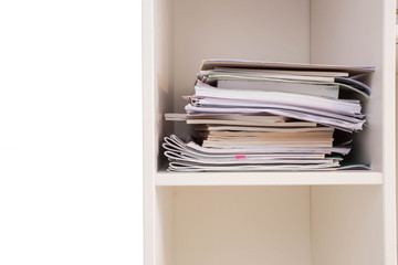 Pile of documents on a wooden shelf stack up high waiting to be managed, closet closeup