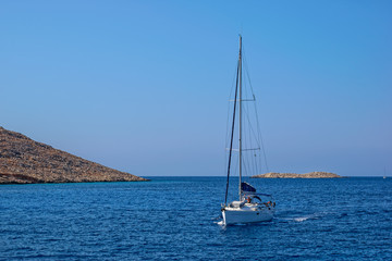 Obraz premium A sailing yacht crosses Emborio harbour on the Greek island of Halki (Chalki).
